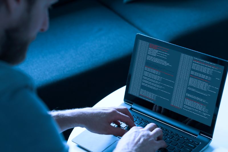 Operatore informatico davanti a un laptop con codice e alert di sicurezza, durante attività di monitoraggio cybersecurity e prevenzione phishing.