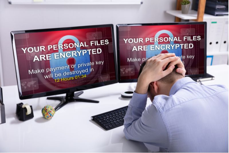 Dipendente di un'azienda davanti a due monitor con una richiesta di riscatto dopo un attacco ransomware. Dipendente di un'azienda davanti a due monitor con una richiesta di riscatto dopo un attacco ransomware.